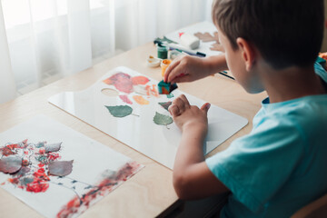 Cute child sitting at desk and making picture from dry birch leaves