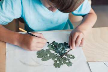8 years old child siting by desk and doing herbarium on album sheet