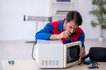 Young male repairman repairing oven at workshop
