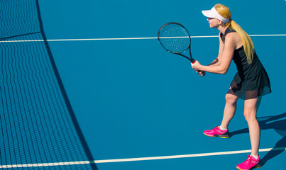 Fototapeta na wymiar A girl plays tennis on a court with a hard blue surface on a summer sunny day