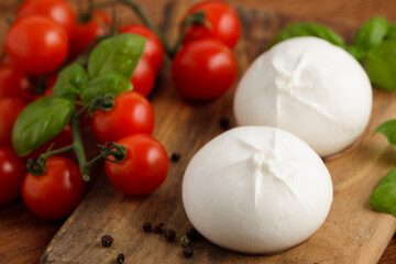 Fresh Italian burrata with tomatoes and basil on wooden cutting board, close up. Burrata cheese ball made from mozzarella and cream. Healthy food