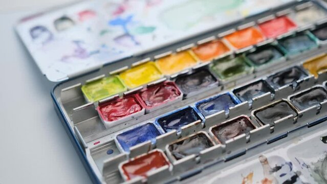 Woman hand opening used old watercolor palette with different colors. Colorful aquarelle set for art creation and painter