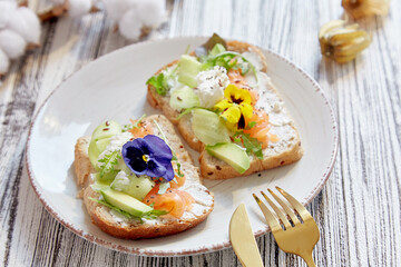Aesthetic toasts with smoked salmon, avocado, cucumber and edible flowers. Pescetarian diet. Healthy appetizer