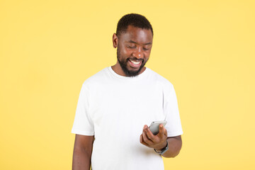 Black Man Using Phone Standing Over Yellow Background In Studio