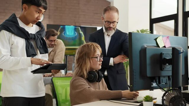 Caucasian woman artist designer draws on a computer tablet 3d models for games. A company director is discussing a project with an Asian developer in the studio.