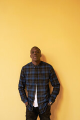 Man in checked shirt with hands in pockets over yellow background.