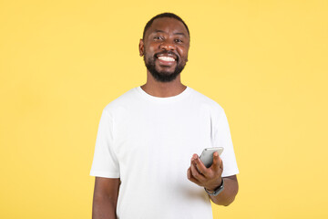 Positive Black Guy Using Smartphone Texting Standing On Yellow Background