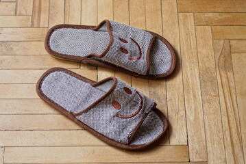 two gray fabric slippers stand on a brown wooden parquet floor in a room