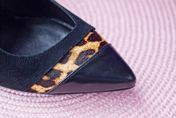 a piece of a black single leather shoe with a brown stripe of spotted wool stands on a pink table