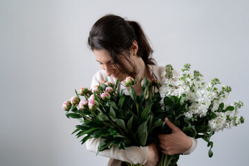WOMAN florist EMBRACING a bunch of white and pink flowers on white background indoors