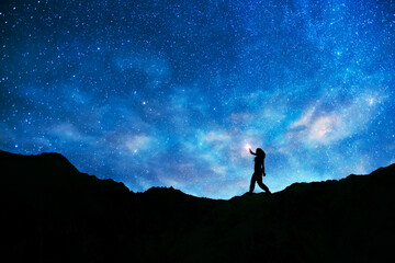Girl silhouette stands on the hill on and looks on the  milky way galaxy. Dark starry night.