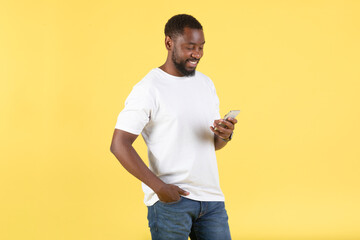 African American Guy Using Smartphone Browsing Internet Over Yellow Background