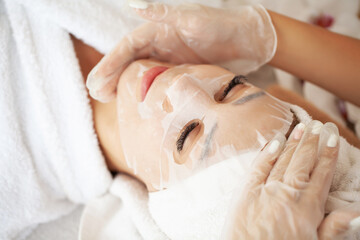 Obraz na płótnie Canvas Young woman with cloth mask at spa salon