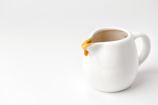 Drop of liquid caramel on a white gravy boat on grey background.