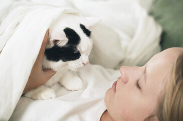 A teenager girl lies with a cat under a blanket, stroking him