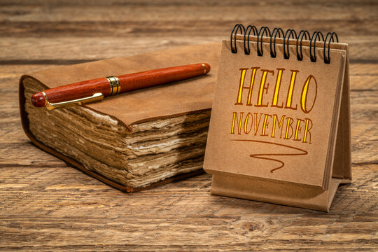 Hello November welcome note  - handwriting in a spiral sketchbook or calendar on a rustic wooden table with a retro journal