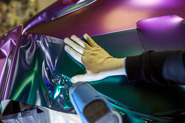 A specialist in wrapping a car with chameleon-colored vinyl film in the process of work. Car wrapping specialists cover the car with vinyl sheet or film. Selective focus.