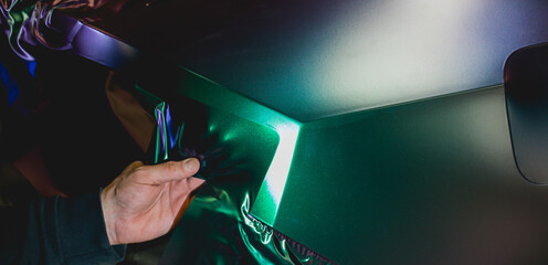 A specialist in wrapping a car with chameleon-colored vinyl film in the process of work. Car wrapping specialists cover the car with vinyl sheet or film. Selective focus.