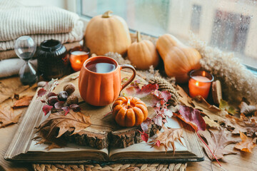 Obraz na płótnie Canvas Autumn still life on the windowsill, a cup of tea, candles, pumpkins, leaves, thanksgiving house interior