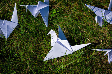 Japanese folded Origami cranes on fresh grass. Hundreds handmade paper birds on green field with copy space. 1000 thousand crane tsuru sculpture topic. Symbol of peace, health, wishes and hope