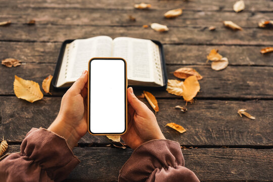 Open bible and phone with isolated screen on wooden background