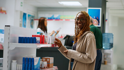 Smiling african american woman checking boxes of medication on pharmacy shelves, looking at...