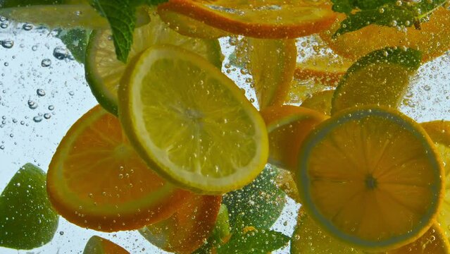 Pieces citrus fruit dropped with mint in water closeup. Sliced orange lemon lime