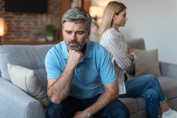 Unhappy middle aged european man ignores offended lady after quarrel in living room interior