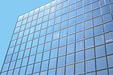 Fototapeta na wymiar Glass building full of windows against blue sky- photographed from an angle - Great blue tech background with interesting reflections on glass