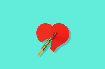 scissor cuts red paper heart, rupture concept, on aquamarine background.
