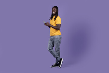Fototapeta na wymiar Cool african american guy using cell phone on purple
