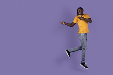 Fototapeta na wymiar Happy black guy jumping, pointing at copy space on purple