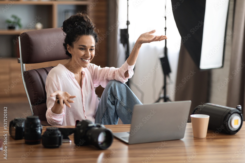 Wall mural Creative young woman photographer having video call, using laptop