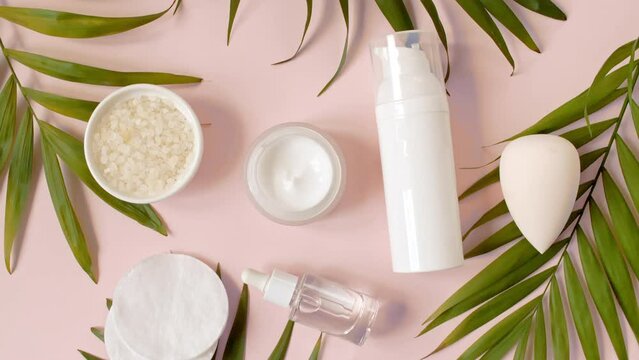 Natural cosmetics, skin care products. Bottle with pipette with gel, fluid, collagen serum, oil, cream, lotion, soap, sponge on a pink background with green palm leaves. Organic cosmetics. flat lay.4k
