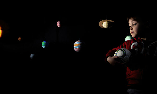 Menino com uma bola de futebol embaixo dos braços ao lado de planetas feitos de isopor. - Powered by Adobe