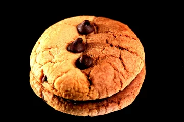 Tuinposter Closeup shot of a chocolate chip cookie isolated on a black background © Mike Campbell/Wirestock Creators