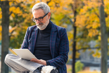 Elegant retired caucasian man with eyeglasses and gray hair and gray facial hair reading a book on...