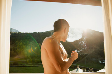 Shirtless guy smoking a marijuana joint on the terrace in the morning