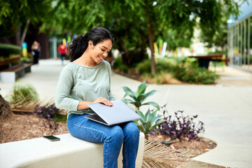 Smiling female freelancer closing laptop while sitting on bench