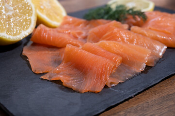 Slices of tasty smoked Scottish salmon fish served on black plate with lemon and fresh dill