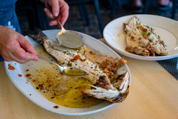 Serving in restaurant of fresh grilled on old charcoal parrillas sea bass fish in small fisherman's village Getaria, Basque Country, Spain