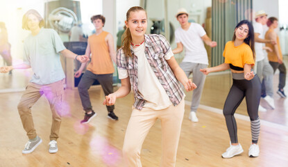 Cheerful teen girl enjoying while training movements of modern group dance in choreography class .