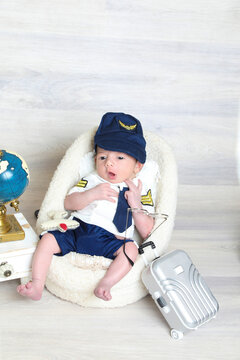 toddler boy in pilot uniform sitting at soft tiny chair,toy suitcase world map,face photography