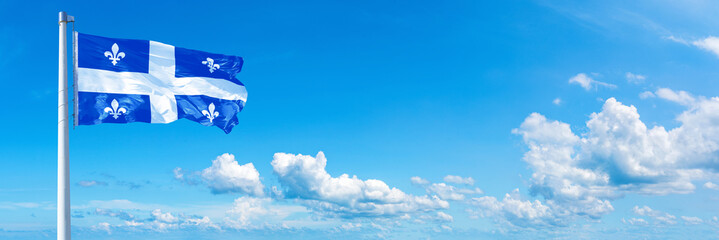 Fototapeta premium Quebec - Canada flag waving on a blue sky in beautiful clouds - Horizontal banner 