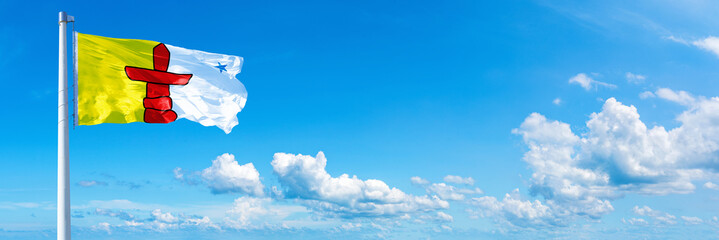 Nunavut - Canada flag waving on a blue sky in beautiful clouds - Horizontal banner
