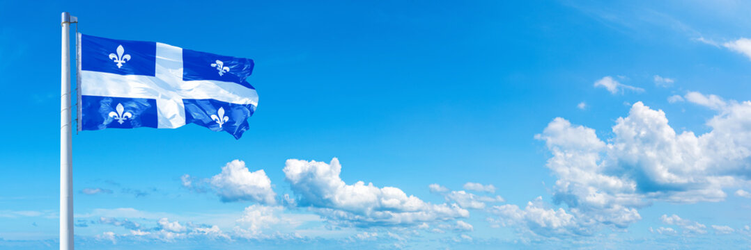 Quebec - Canada flag waving on a blue sky in beautiful clouds - Horizontal banner
