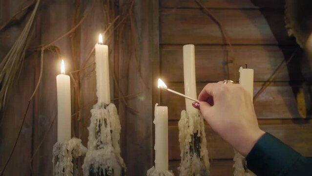 A fortuneteller's hand lights candles on the altar for an esoteric ritual, wax flows across the candlestick