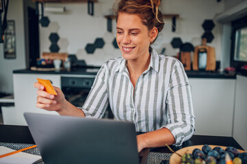 Young woman using laptop and a credit card in the kitchen at home