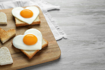 Heart shaped fried eggs with toasts on white wooden table, closeup. Space for text