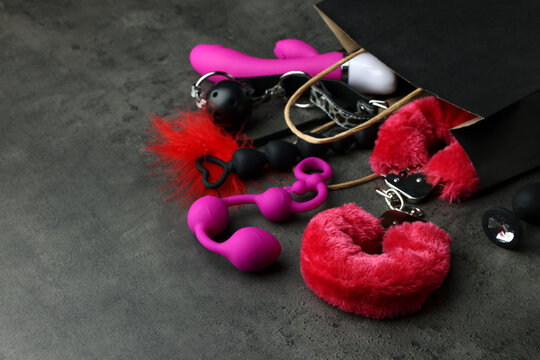Paper shopping bag with different sex toys on grey table. Space for text
